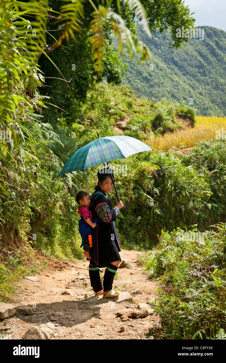 Woman from the Black H'mong tribe wearing traditional indigo blue clothing, carrying a baby on her back North Vietnam Stock Photo