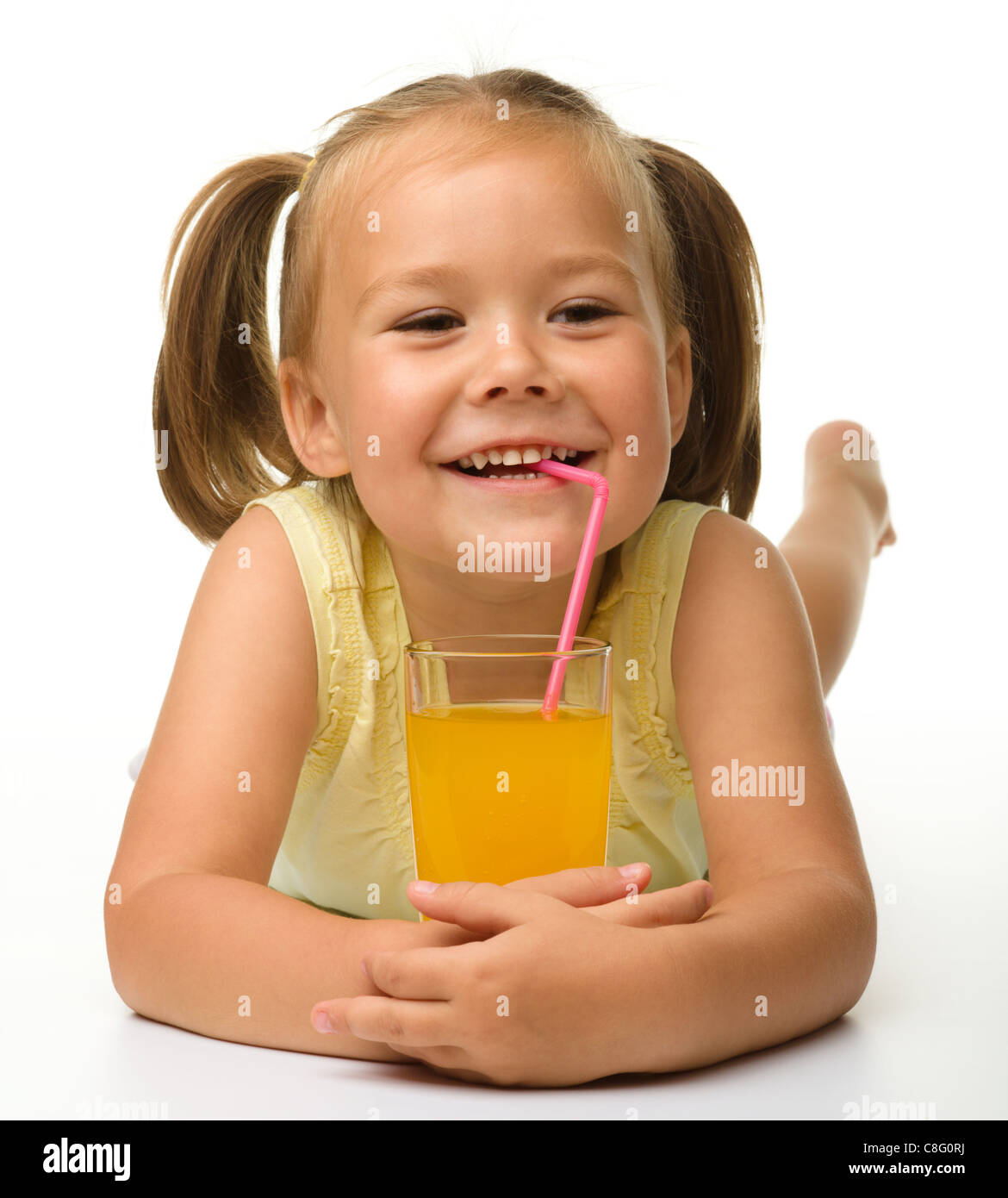 Cute little girl drinks orange juice using drinking straw while laying