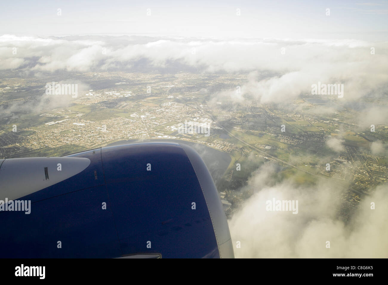 View from passenger aircraft window at  take off, engine in foreground land, fields and roads below through light cloud cover Stock Photo