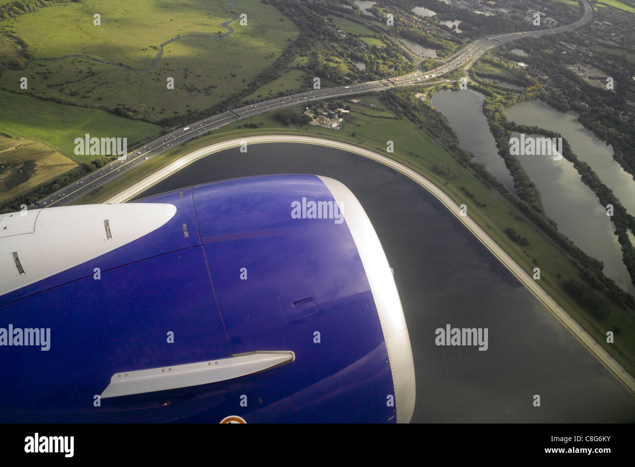 View from passenger jet aircraft window at  take off with engine in foreground and land with fields, water and roads below Stock Photo