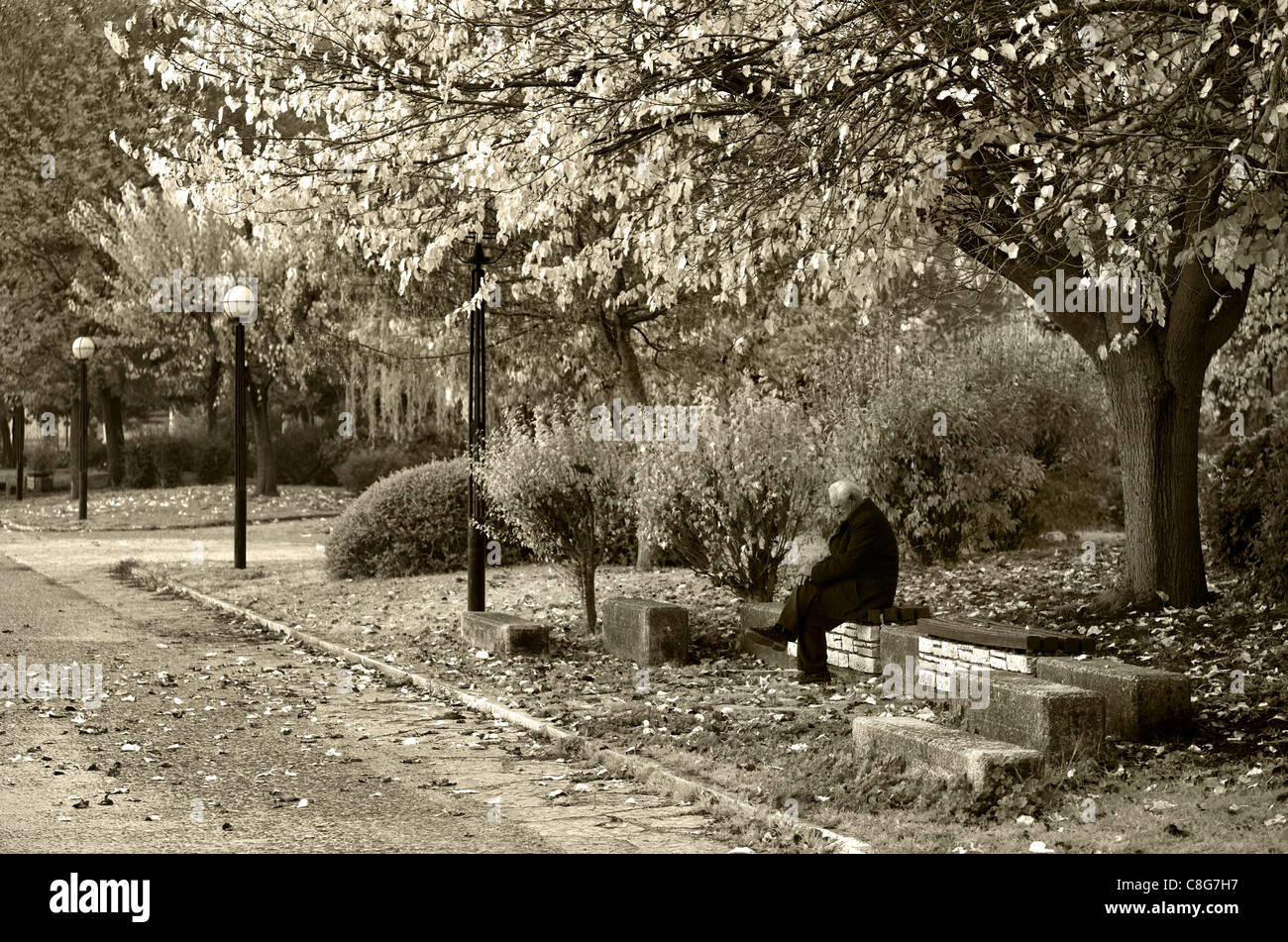 A lonely old man sitting skeptical and melancholic on a bench on the lakeside road of Ioannina, Epirus, Greece (b&w version) Stock Photo