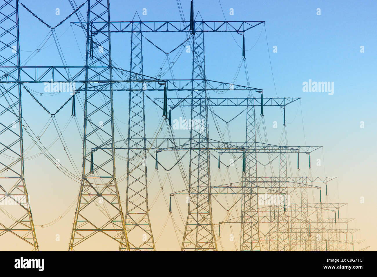 Electricity pylons standing in a row just before sunset Stock Photo