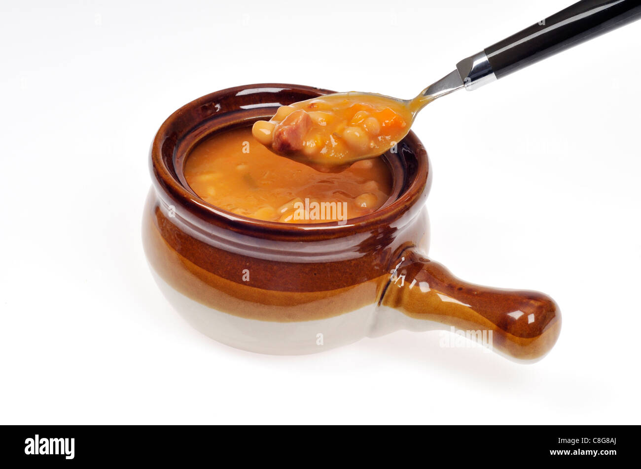 Spoonful and crock of ham & bean soup  with spoon on white background. Stock Photo