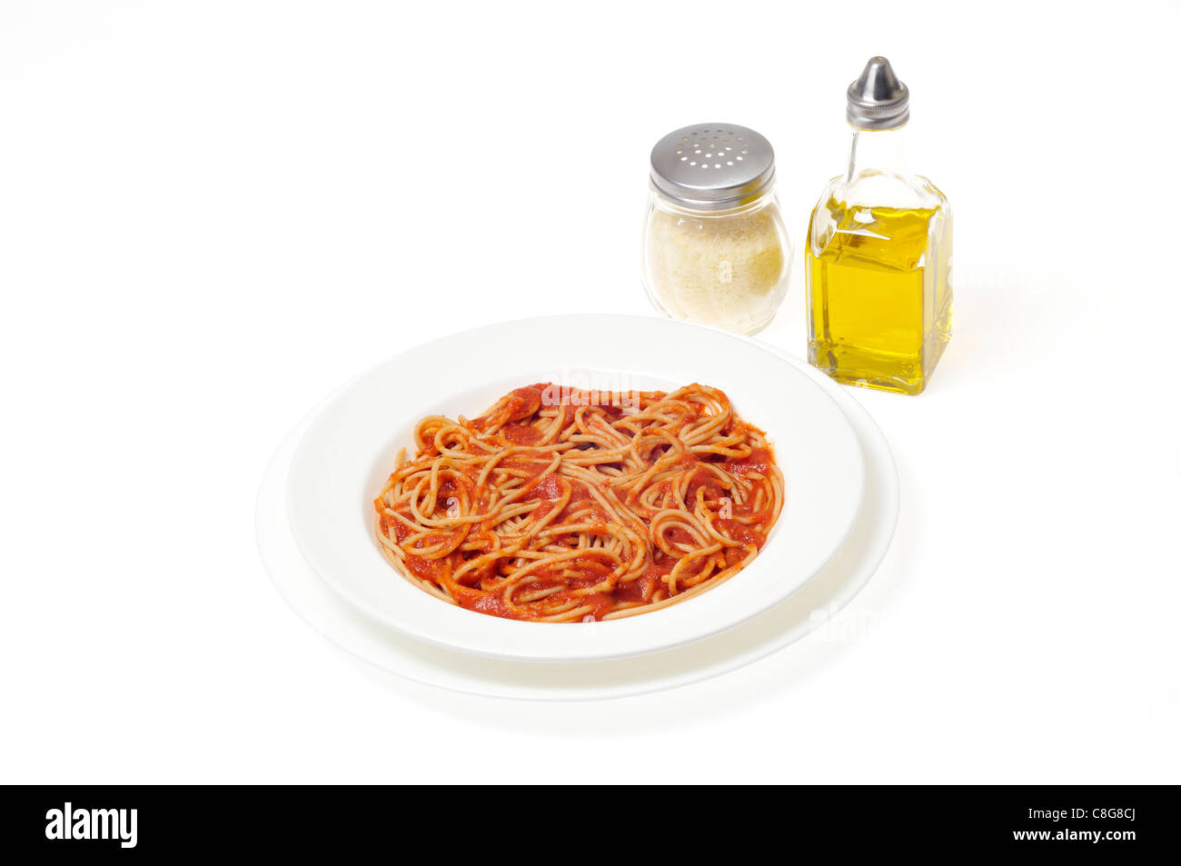 Cooked whole wheat spaghetti in white bowl with condiments of olive oil and grated parmesan cheese jar on white background cutout. Stock Photo