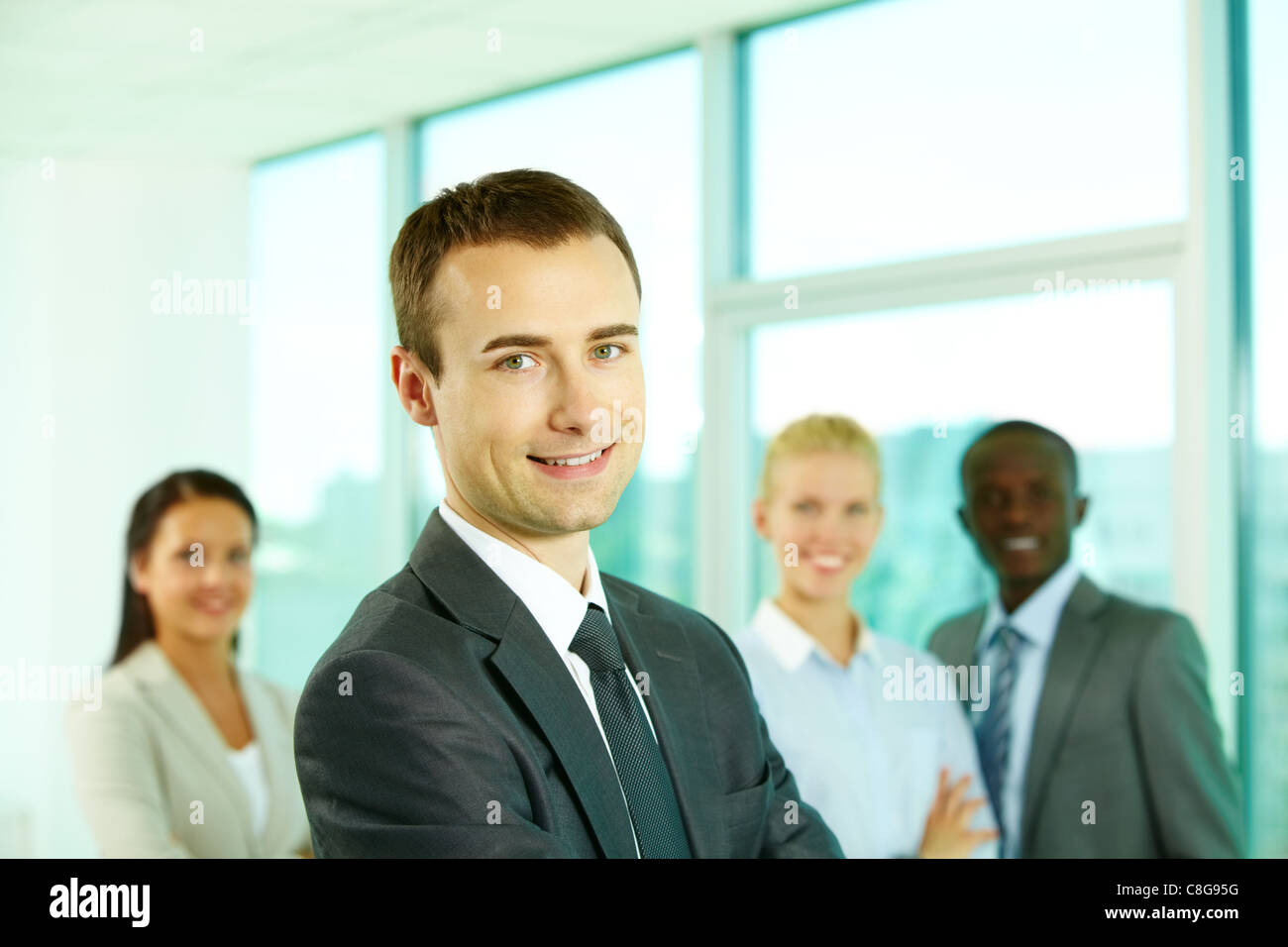 Young man looking at camera and smiling against his team Stock Photo ...