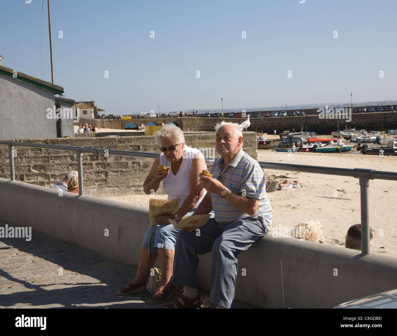 St Ives Cornwall England UK Elderly man and woman sitting on sea wall eating famous Cornish pasties popular seaside resort Stock Photo