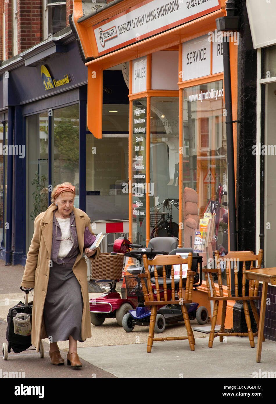 older woman walking past a small shop selling mobility scooters and useful equipment for the elderly Stock Photo