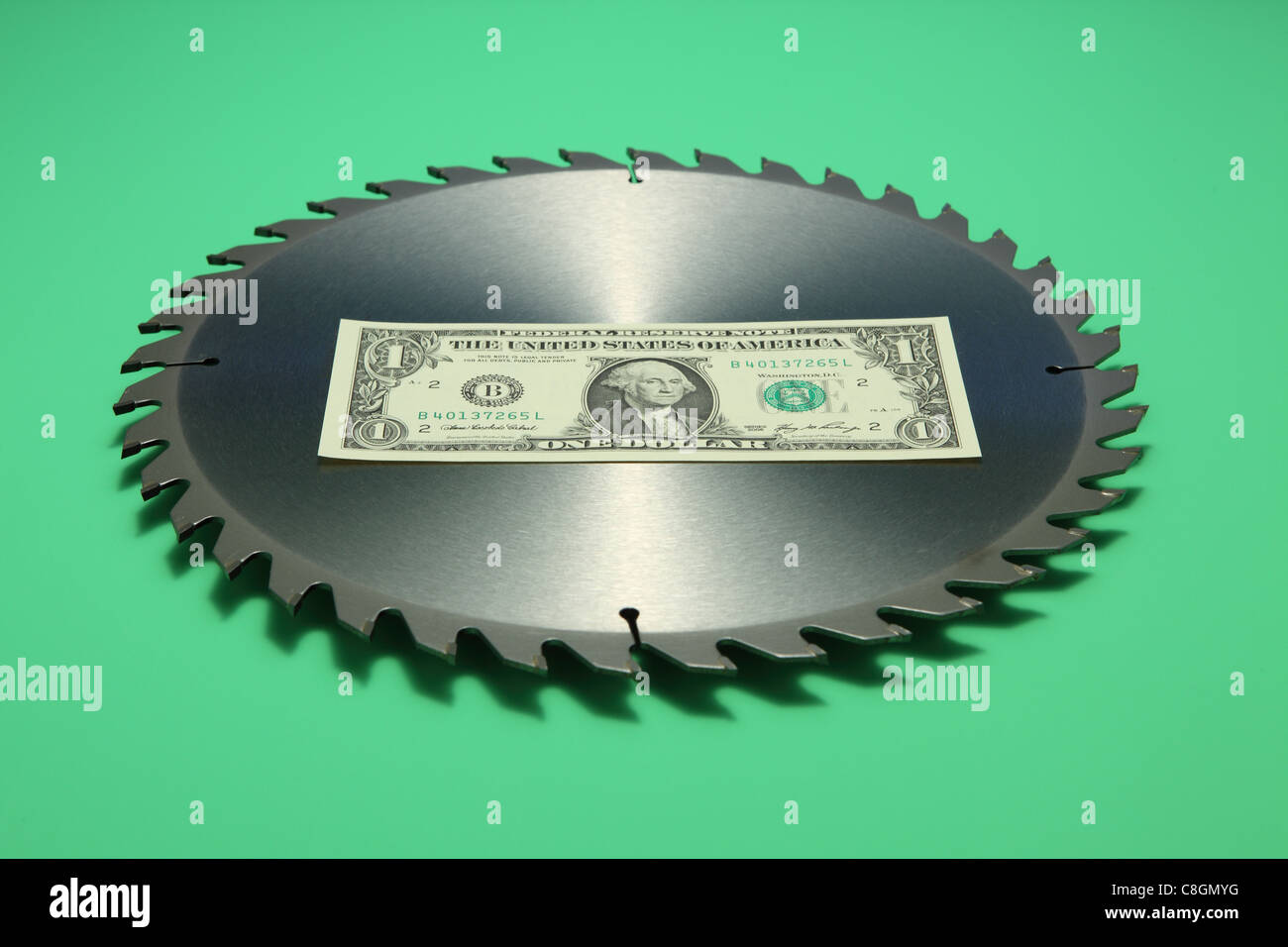 One US dollar banknote in the middle of a metal circular saw blade. Bright green background, banknote front facing Stock Photo