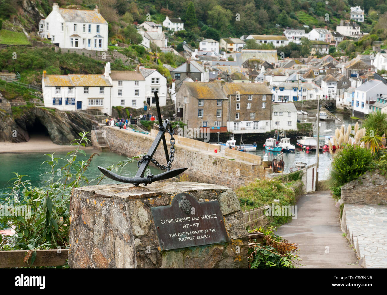 Mounted anchor presented to Polperro by British Legion, with view of village in background, Cornwall UK Stock Photo