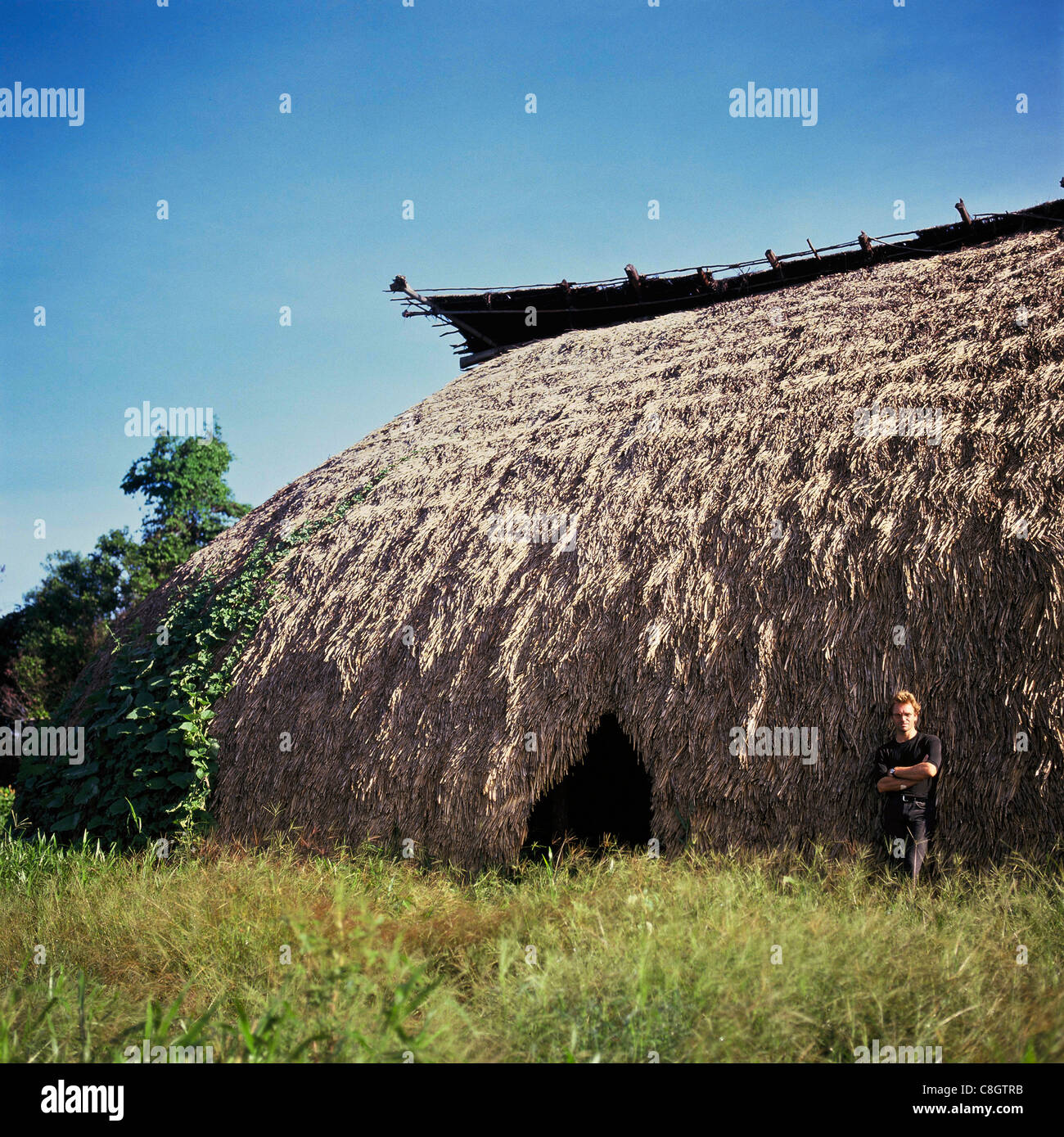 Pavuru Village, Brazil. Sting standing outside a large malloca; Xingu Indigenous reserve, Para & Goias State. Stock Photo
