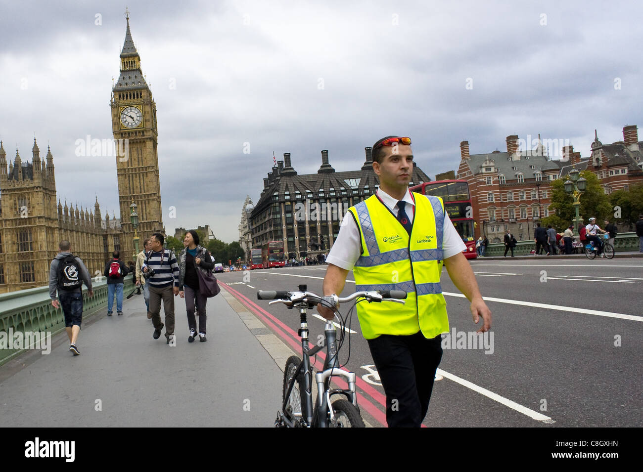 A man in work uniform and a high visibility vest walks his bike across Westminster Bridge in London Stock Photo