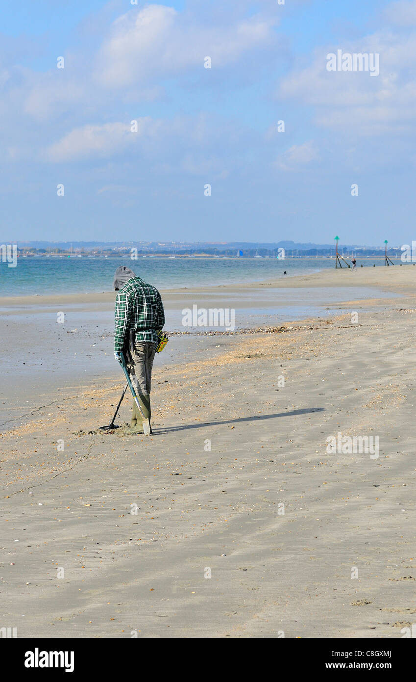 Man with metal detector  looking for lost valuables  on West Wittering beach  after the weekends crowds had departed - West Sussex, England, UK Stock Photo