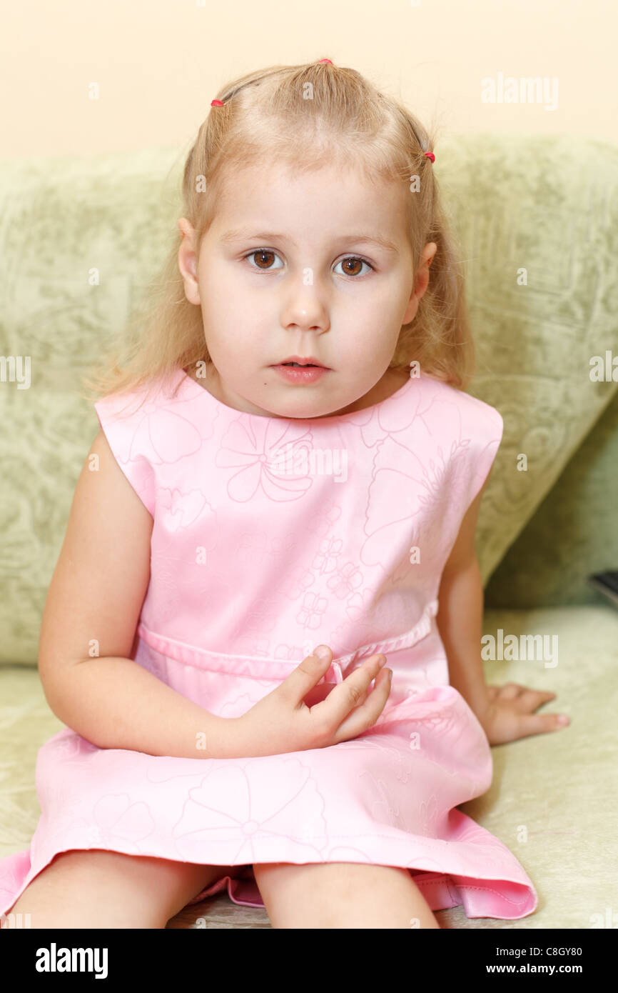 Little child a girl in pink dress sitting on sofa in domestic room. One ...
