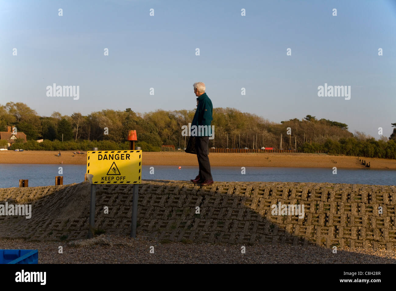 A couple stand on sea defences next to a 'Danger Keep Off' sign at Felixstowe Ferry in Suffolk Stock Photo