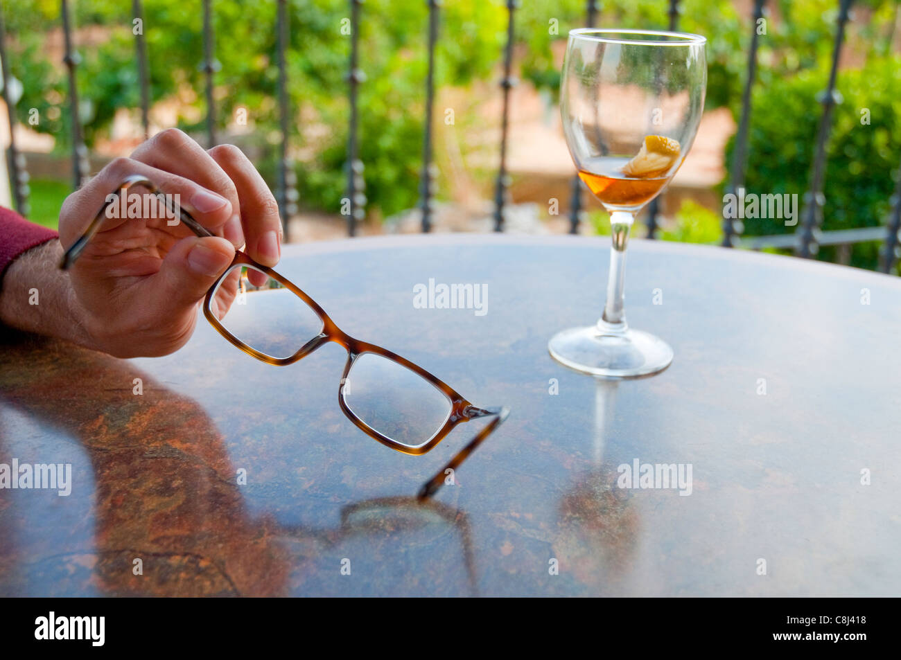 Man's hand holding spectacles and empty glass of liqueur. Stock Photo