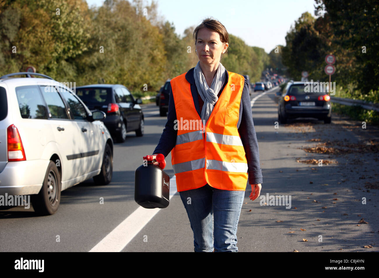 Car breakdown, out of fuel, empty tank. Female driver, is walking with a spare can to the next service station, to get fuel. Stock Photo