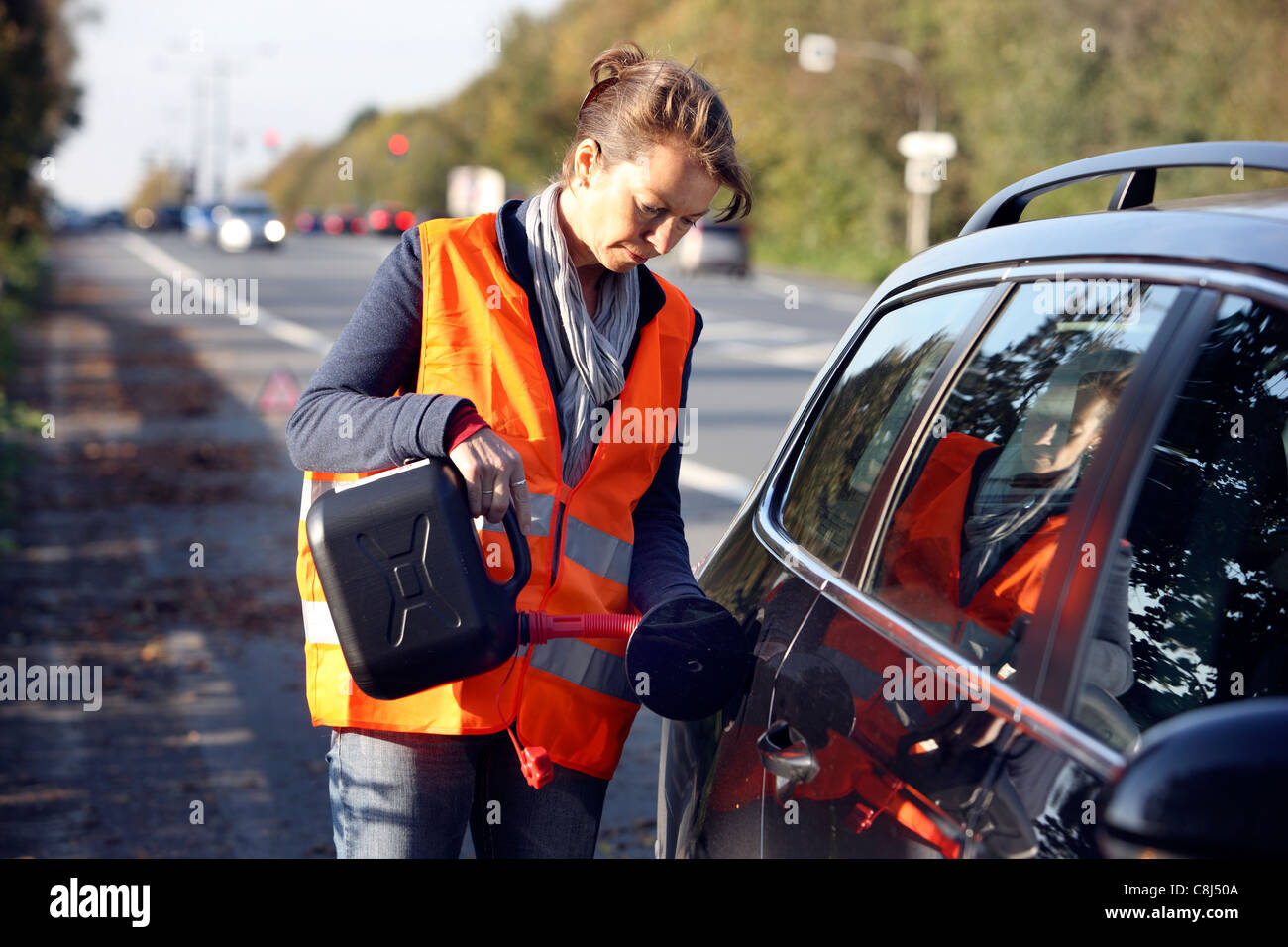 Car breakdown, out of fuel, female driver is refueling the car with a spare can. Stock Photo