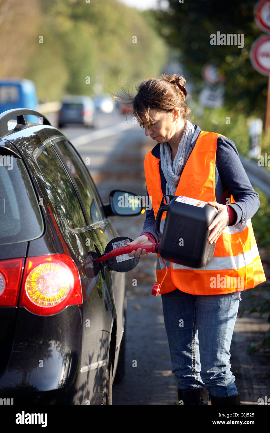 Car breakdown, out of fuel, female driver is refueling the car with a spare can. Stock Photo