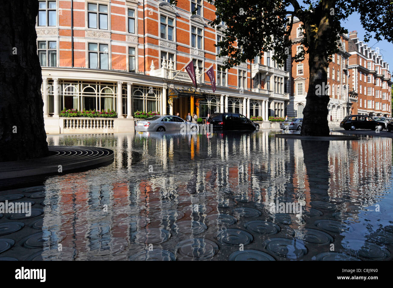 Trees in raised shady water feature pond by Tadao Ando reflection front of luxury Connaught Hotel exterior buildings & cars Mayfair London West End UK Stock Photo