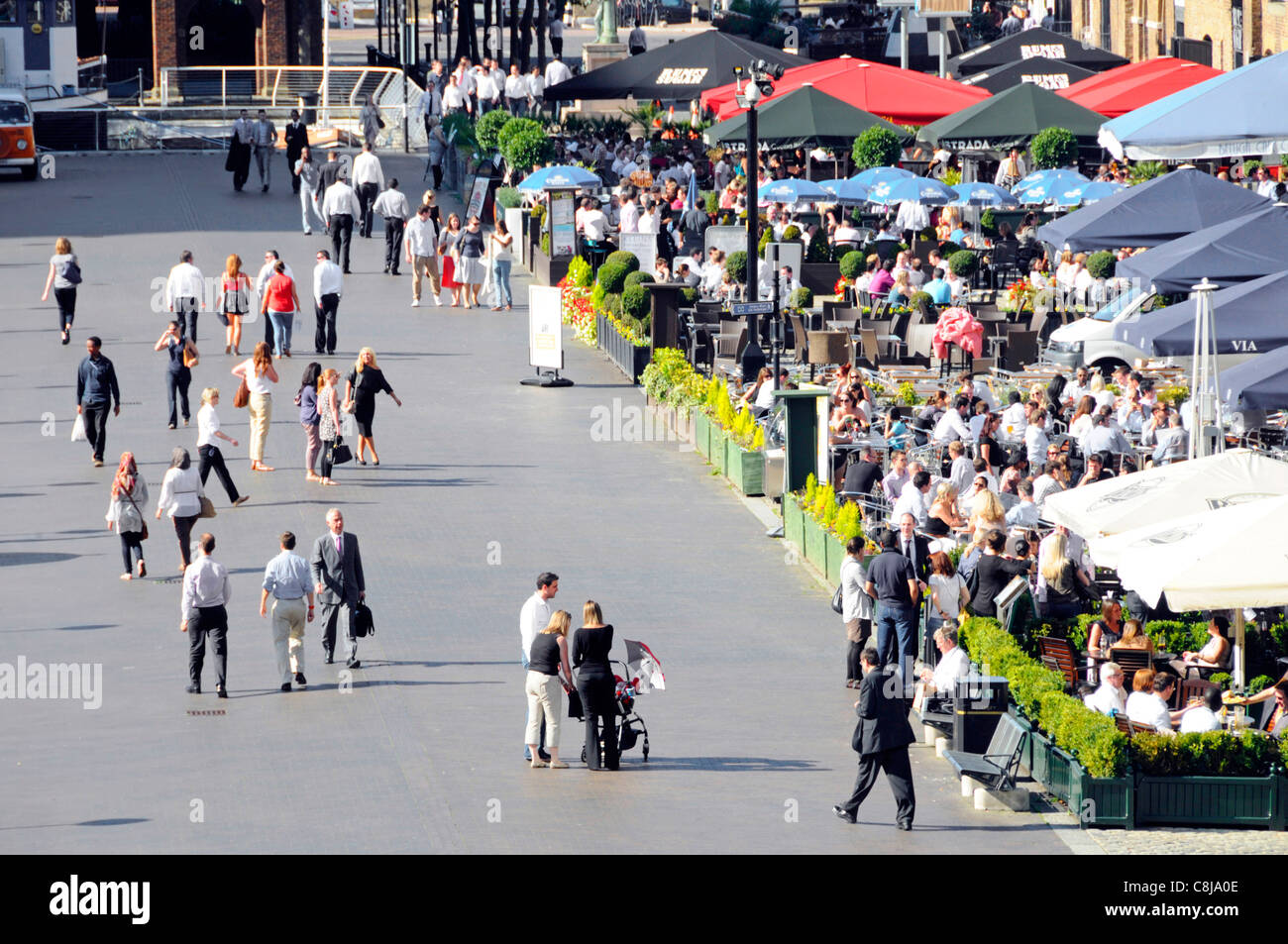 Crowds of office workers eating out at busy outdoor restaurant colourful parasols West India Quay Canary Wharf East London Docklands Tower Hamlets UK Stock Photo