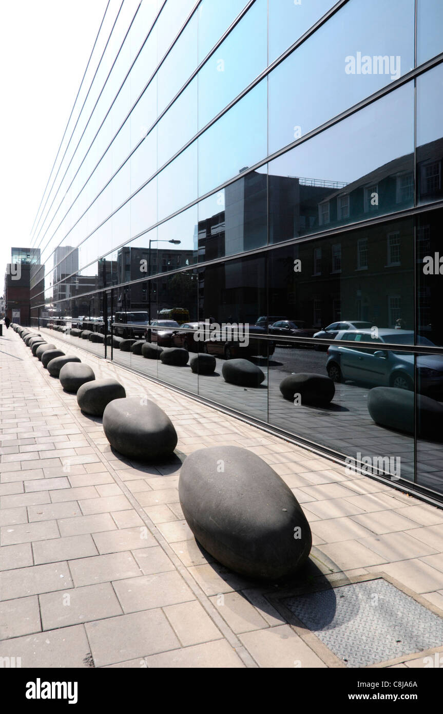Boulders as bollards on pavement in London street scene reflection in