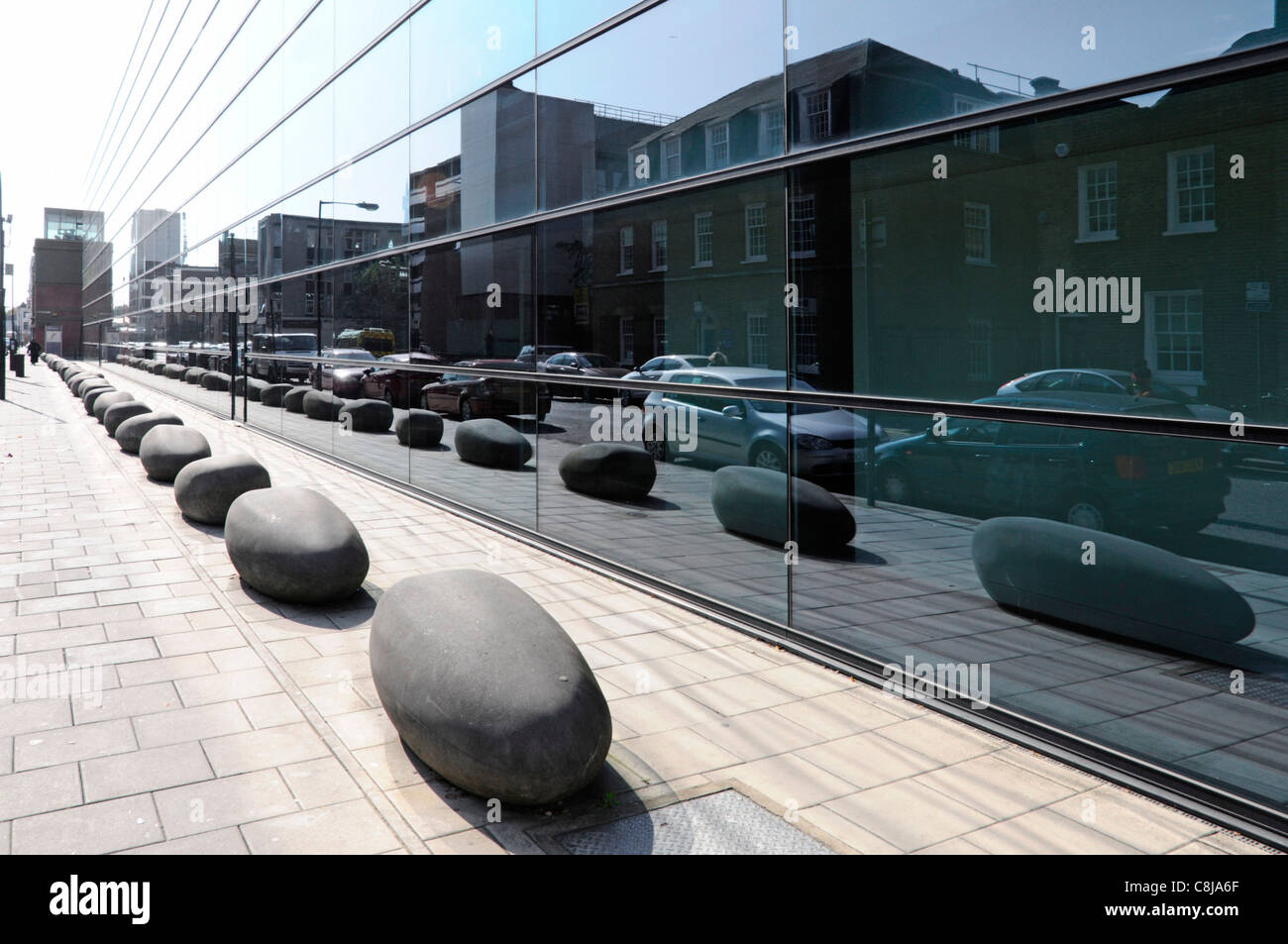 Boulders as bollards on pavement in London street scene reflection in