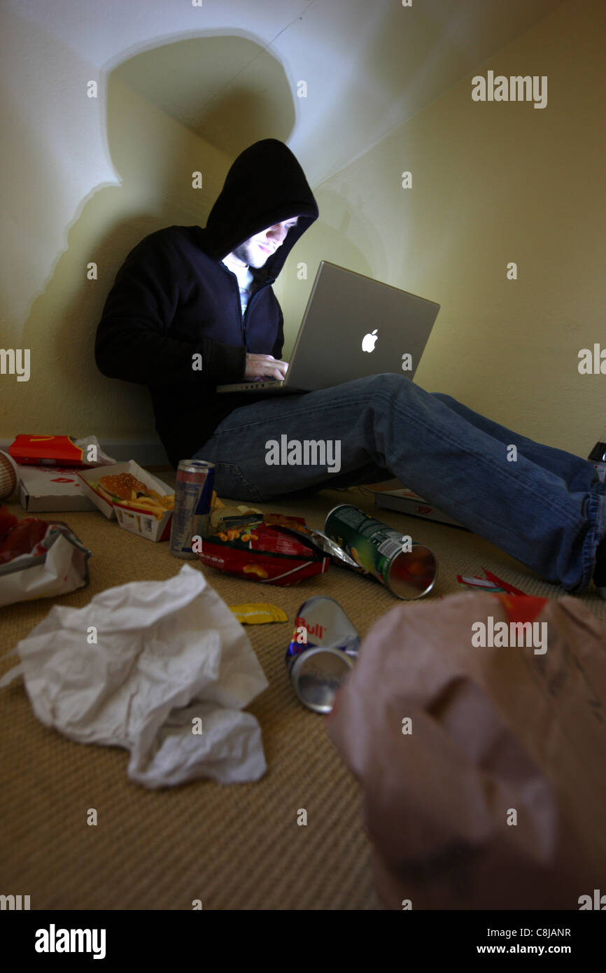 Computer user, hacker, sits conspiratorially, in an empty apartment,  with a laptop. Symbol picture, computer-Internet crime. Stock Photo