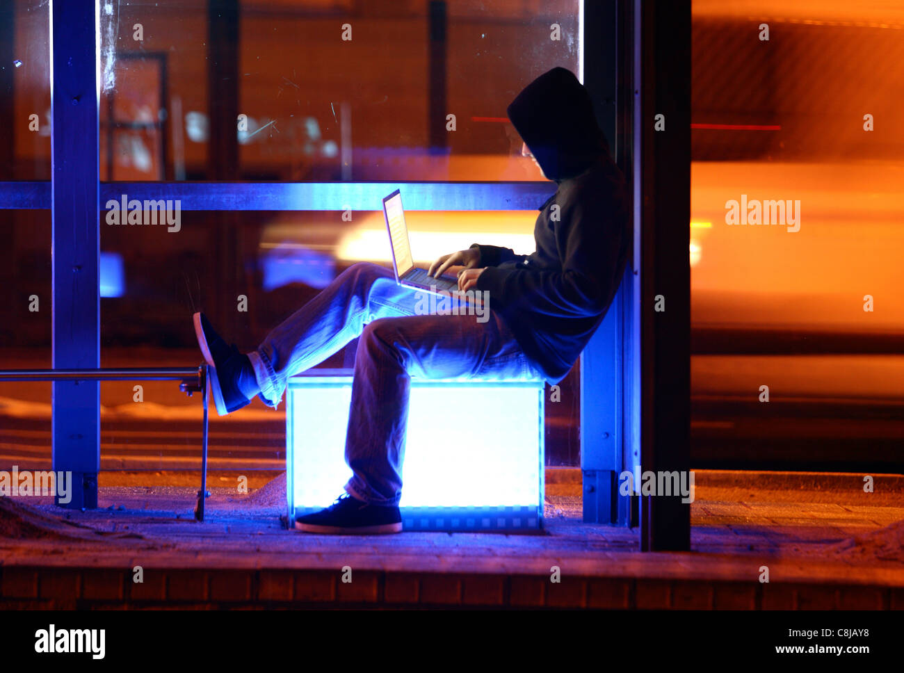 Computer user, hacker, sits conspiratorially, outside,  bus stop,  with a laptop. Symbol picture, computer-Internet crime. Stock Photo