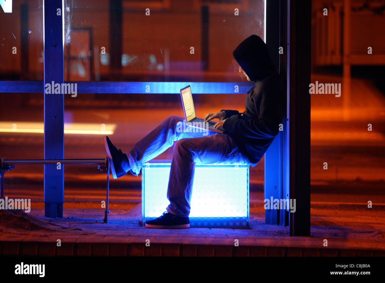 Computer user, hacker, sits conspiratorially, outside,  bus stop,  with a laptop. Symbol picture, computer-Internet crime. Stock Photo