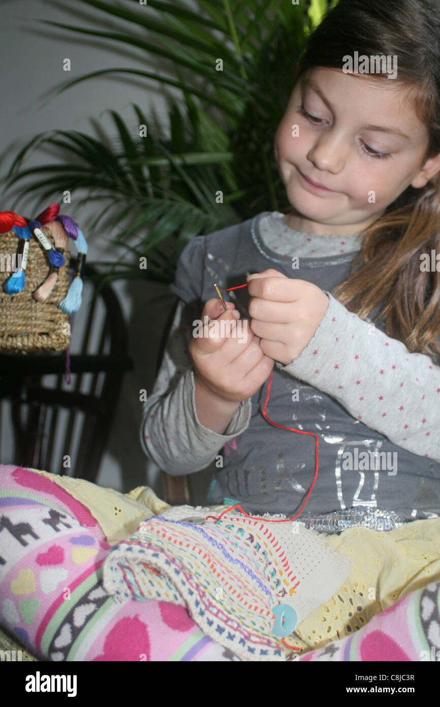 Young girl threading a needle sewing on aida panel , UK , England Stock Photo