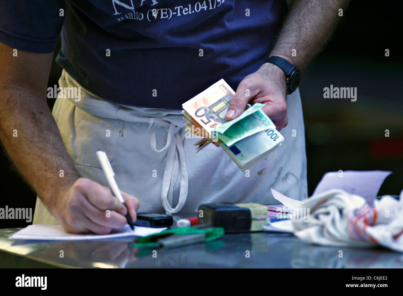 Man counting the days takings in euros to his ledger, Venice Italy Stock Photo