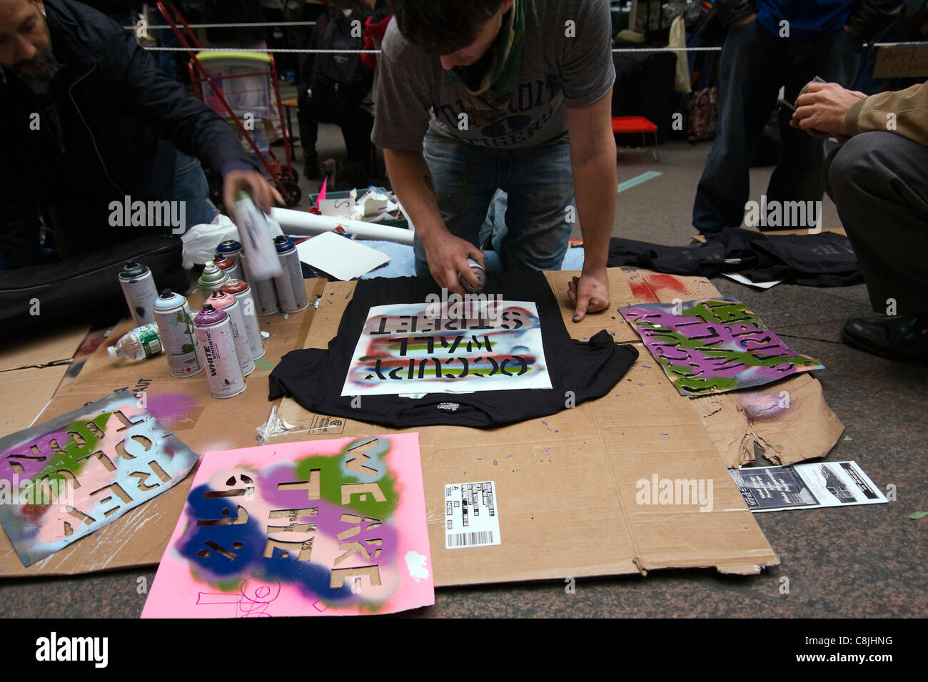 Occupy Wall Street protester spray painting 'OCCUPY WALL STREET' on a black T-shirt inside of Zuccotti Park Stock Photo