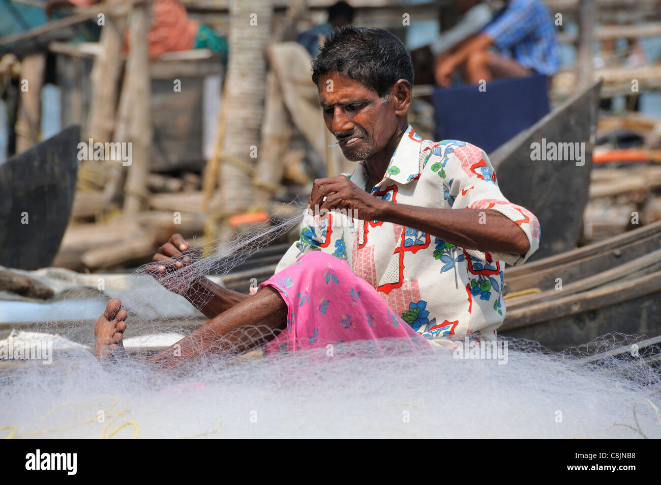 Indian fisherman mending his nets on the banks of Cochin's famed harbour, at Fort Cochin, also known as Fort Kochi,  Kerala, India Stock Photo