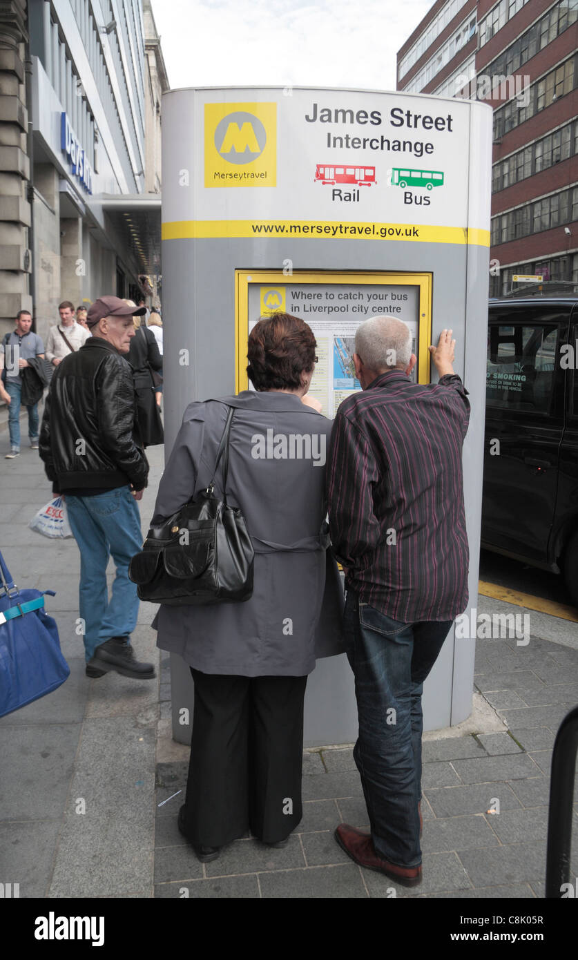 A couple look at the bus/rail interchange timetable on James Street, Liverpool, UK. Stock Photo