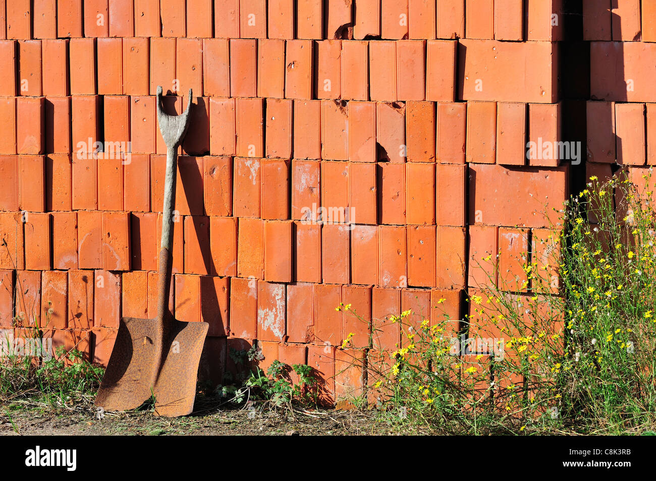 Shovel and pile of stacked red bricks as building material at
