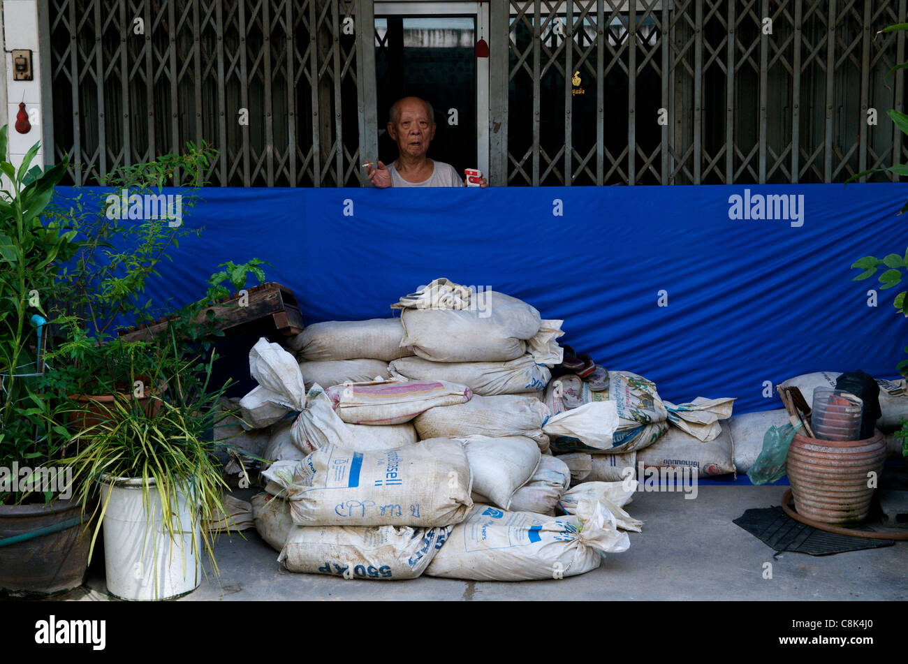 Elderly Bangkok resident prepares for the flood w/ sandbags in front of his shophouse, Sukhumvit Road, Bangkok, Thailand. credit: Kraig Lieb Stock Photo
