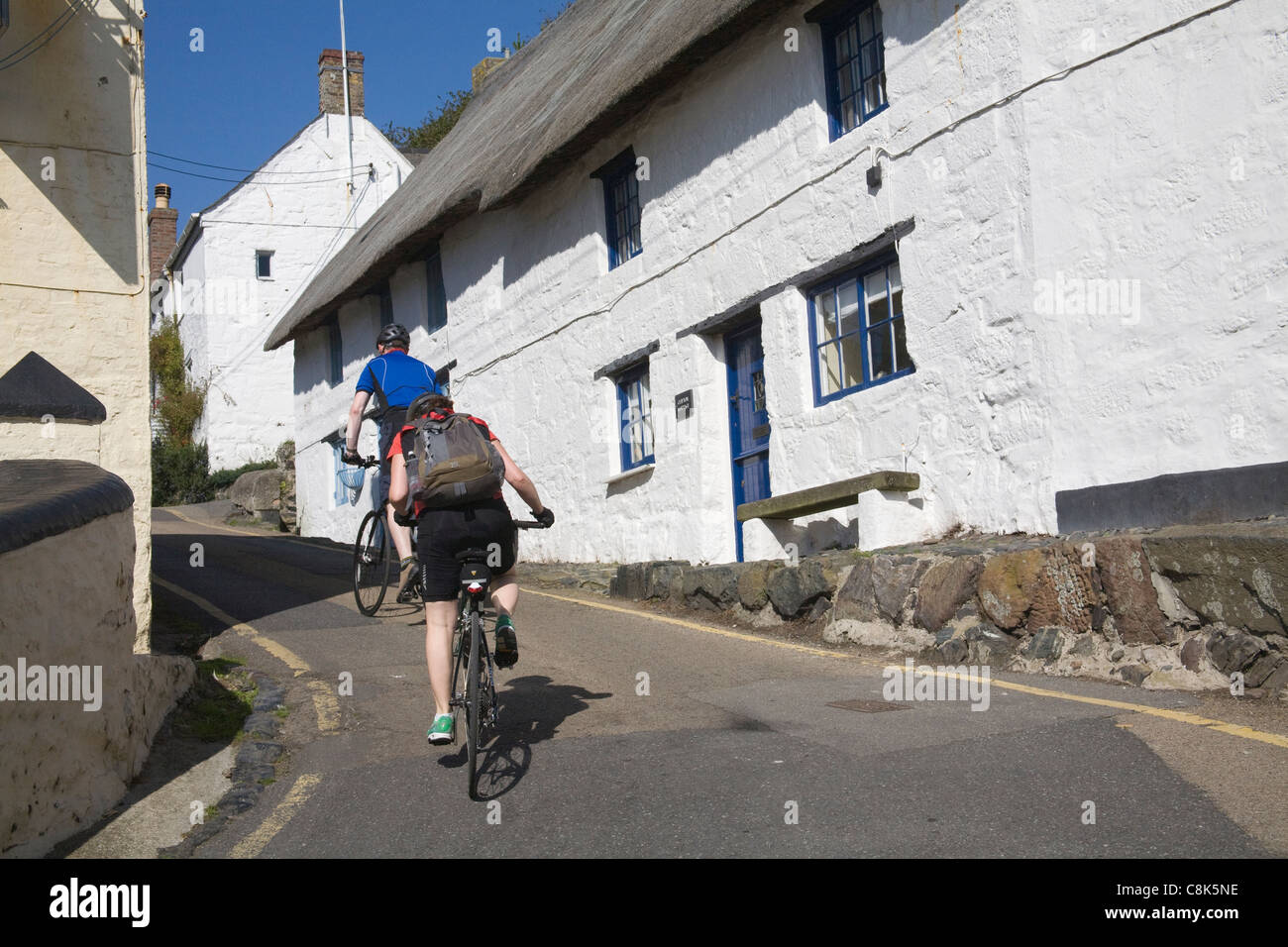 Cadgwith Cornwall England Male and female cyclists leaving picturesque fishing village cycling up steep hill Stock Photo