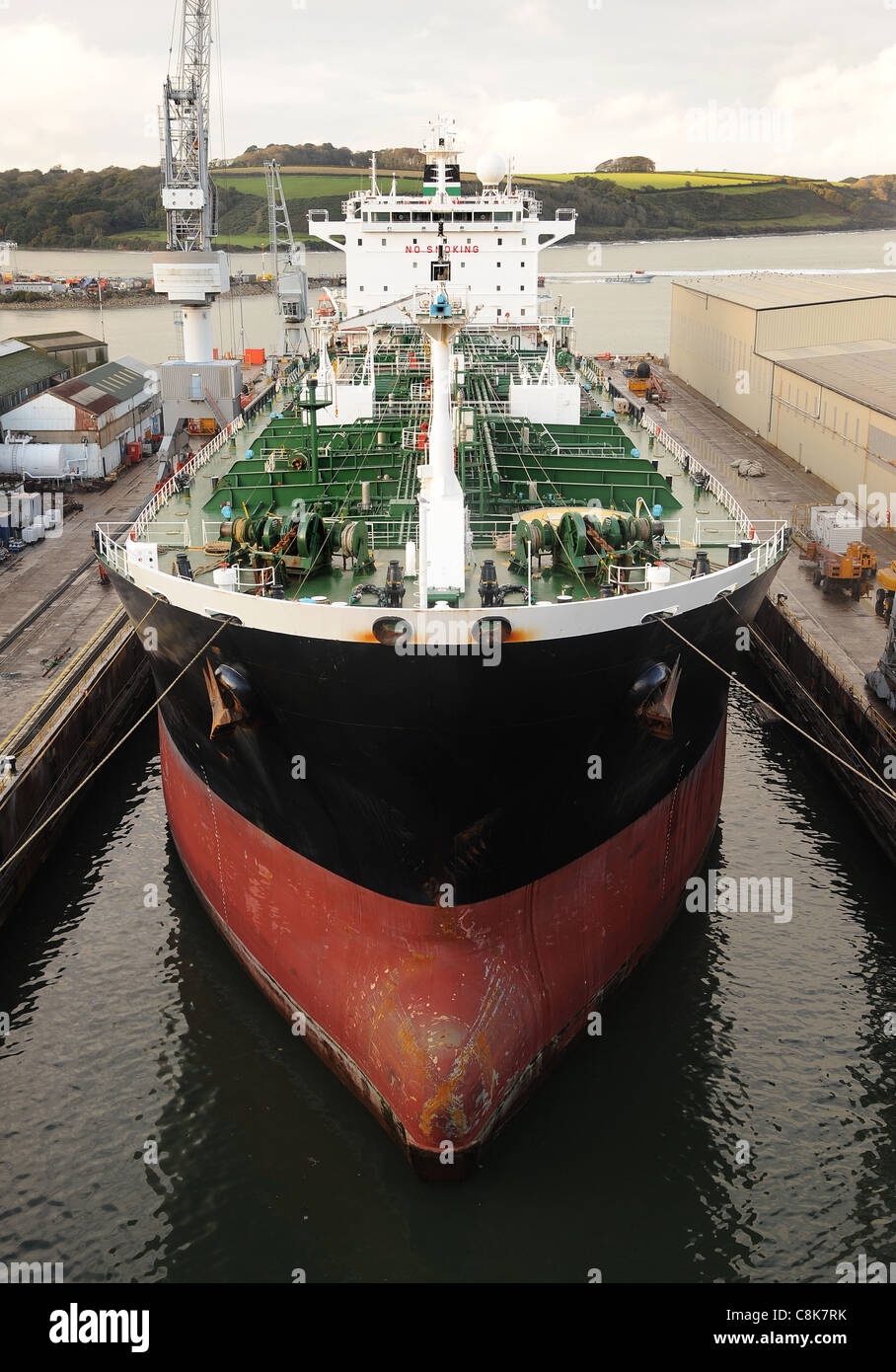 A modern supertanker at rest in a dock. Good view of bows and upper deck from a high angle. With dockside crane and building Stock Photo