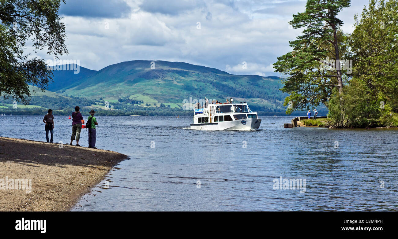 A cruise vessel with tourists is returning towards Balloch in Scotland on river Leven from Loch Lomond in the background Stock Photo