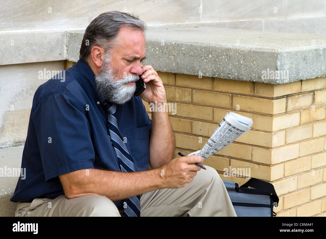 Mature unemployed salesman makes a call on his cell phone to reply to a advertisement for a want ad job in the newspaper. Stock Photo