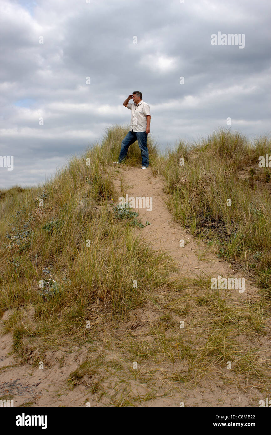 Mature man standing on a sand bank looking out to sea Stock Photo