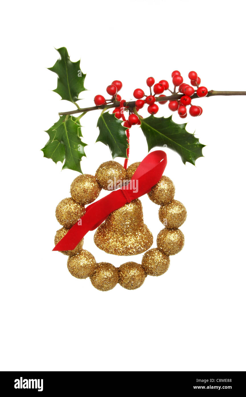 Christmas decoration of gold bell bow and balls hanging from a fruiting holly bough Stock Photo
