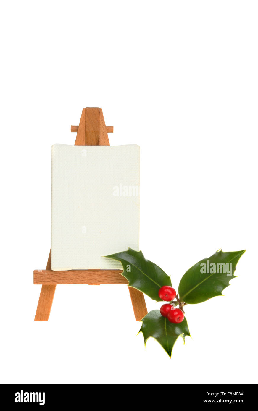 Sprig of fresh holly with berries next to an easel with a blank canvas isolated against white Stock Photo
