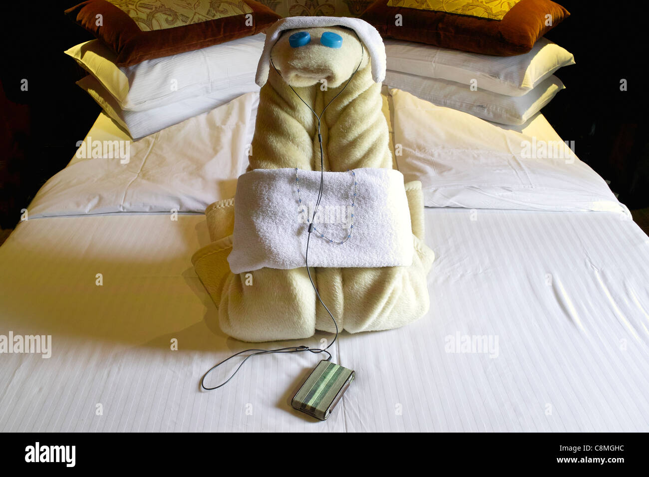 Folded towels making a snake with blue bottle top eyes, wearing headphones, necklace and an mp3 player, arranged on a hotel bed Stock Photo