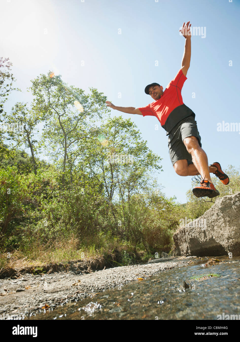 Mixed race man jumping into stream Stock Photo