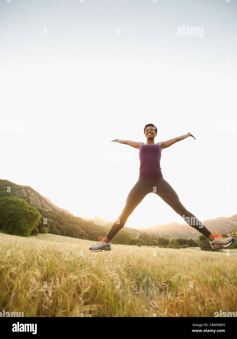 Mixed race woman jumping in remote field Stock Photo
