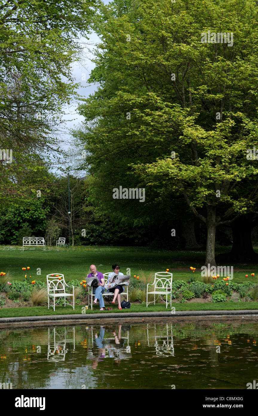 young couple sit sitting read reading relax relaxing around pond farmleigh house phoenix park dublin Stock Photo
