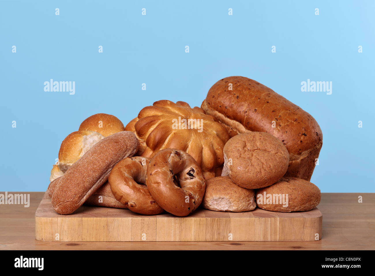 Photo of various types of bread loaves and rolls on a wooden board. Stock Photo