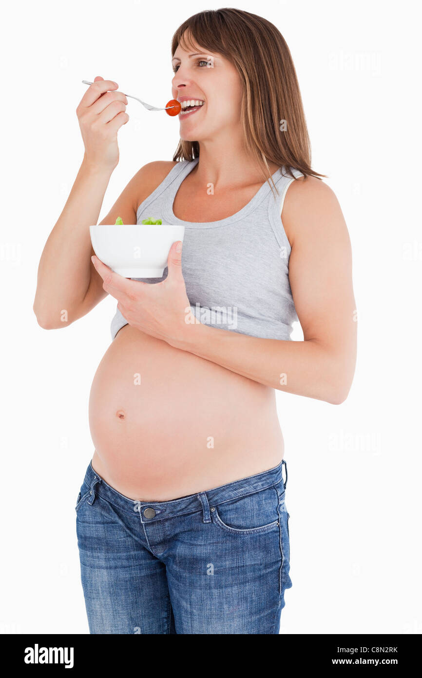 Beautiful pregnant woman eating a cherry tomato while holding a bowl of