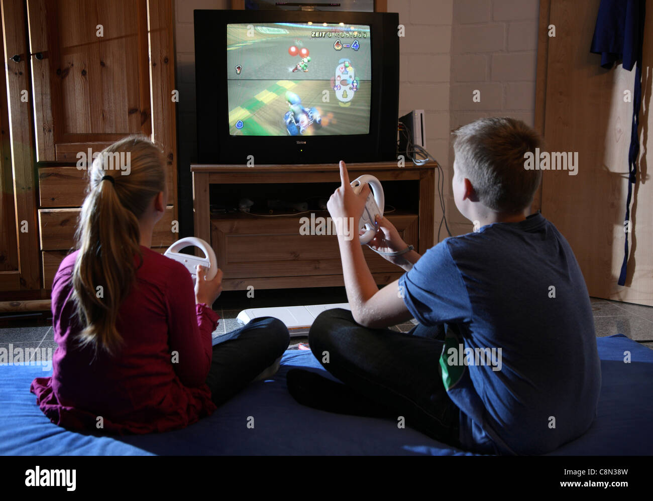 Two kids, girl 10 and boy 13 years old, playing at home with a WII video game. Stock Photo